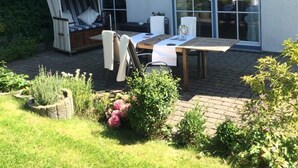 Eine Terrasse mit Tisch und Stühlen, einem Korbsessel und einem gestreiften Sonnensegel.