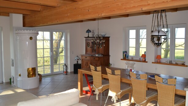 Een ruime eethoek met een houten tafel en stoelen, een open haard en grote ramen met uitzicht op de omgeving.