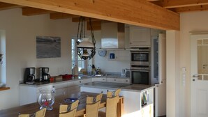 Een moderne keuken met houten balken, een eethoek met rieten stoelen en een groot kookeiland.