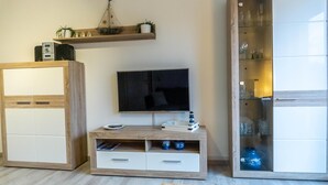 Ein Zimmer mit einem Holzkabinett, einem Fernseher auf einem Schrank und einer Glastruhe mit Dekorationsgegenständen.