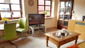 A living room with a television, a green chair, a wooden coffee table, and a yellow sofa.