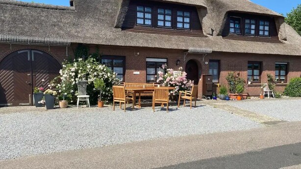 A traditional thatched-roof house with a gravel driveway, wooden furniture, and potted plants.