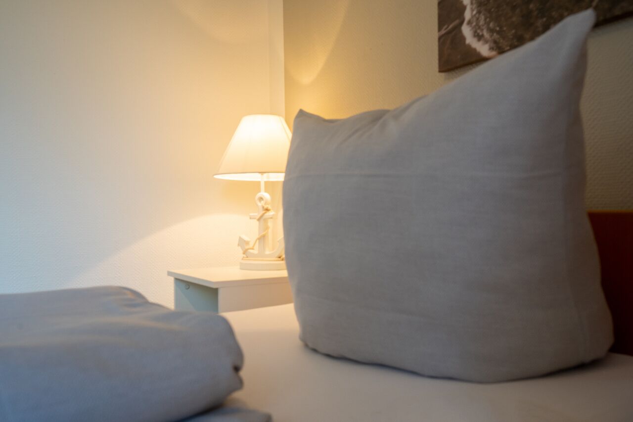 Un lit bien fait, avec un oreiller blanc et une petite table de chevet sur laquelle se trouve une lampe.