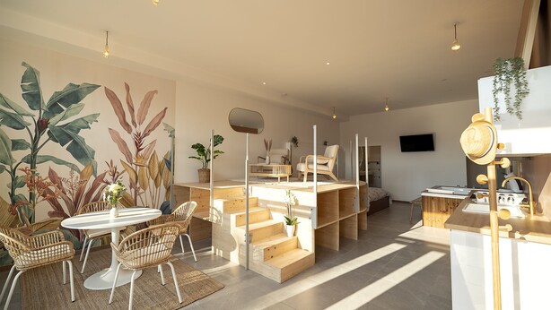 Une cuisine moderne avec des meubles en bois, une cuisinière encastrée et un coin repas comprenant une table ronde et des chaises en osier.