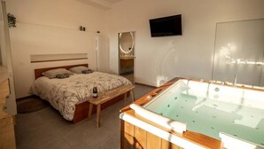 Une chambre avec un lit, une table en bois, un jacuzzi, une télévision et un miroir.