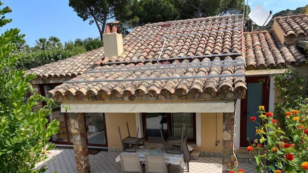 Una casa con techo de tejas, paredes de piedra y un porche cubierto con mobiliario exterior.