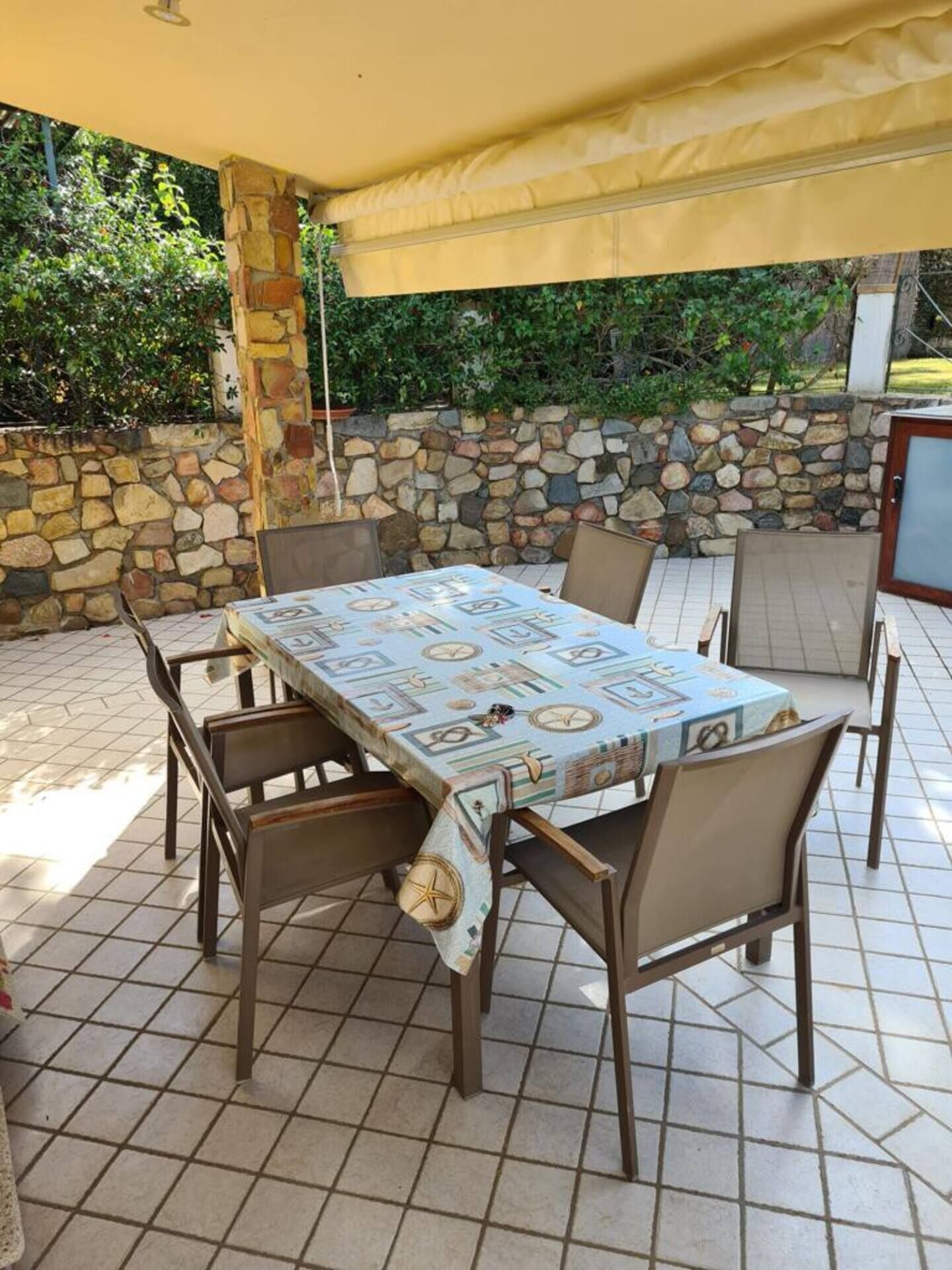 Un patio al aire libre con una mesa, sillas, un muro de piedra y una zona cubierta.