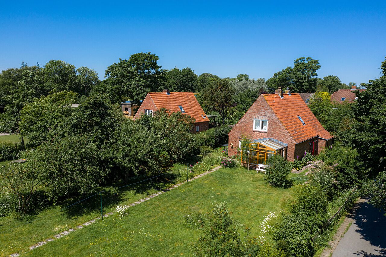 A residential area with houses featuring red-tiled roofs and brick construction, surrounded by lush greenery and trees.