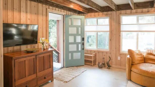 A wooden interior with a television on a cabinet, a door, and a window. - Jus' BeChi A (Folly Beach)