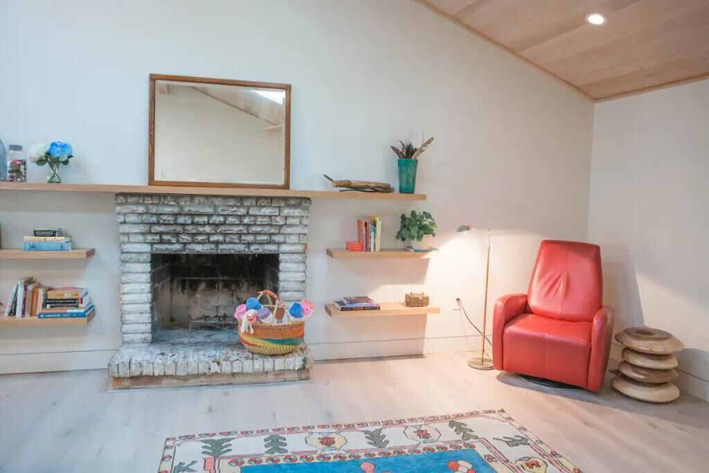 Una sala de estar acogedora con chimenea de piedra, un sillón de cuero rojo y una alfombra estampada.