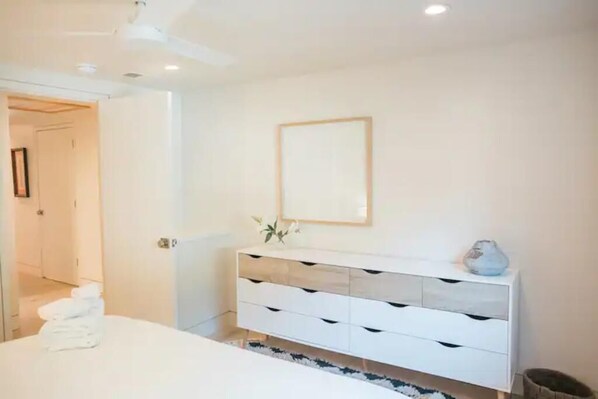 A modern bedroom with a bed, a white dresser, and a framed picture on the wall.