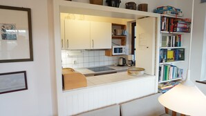 Keittiössä on valkoiset kaapit, mikroaaltouuni, vedenkeitin ja kahvinkeitin. Siellä on myös kirjahylly, jossa on kirjoja, sekä lamppu.