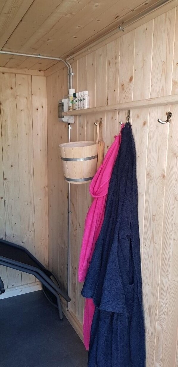 A wooden cabin with a metal shelf holding toiletries, a hanging towel rack, and a metal chair.