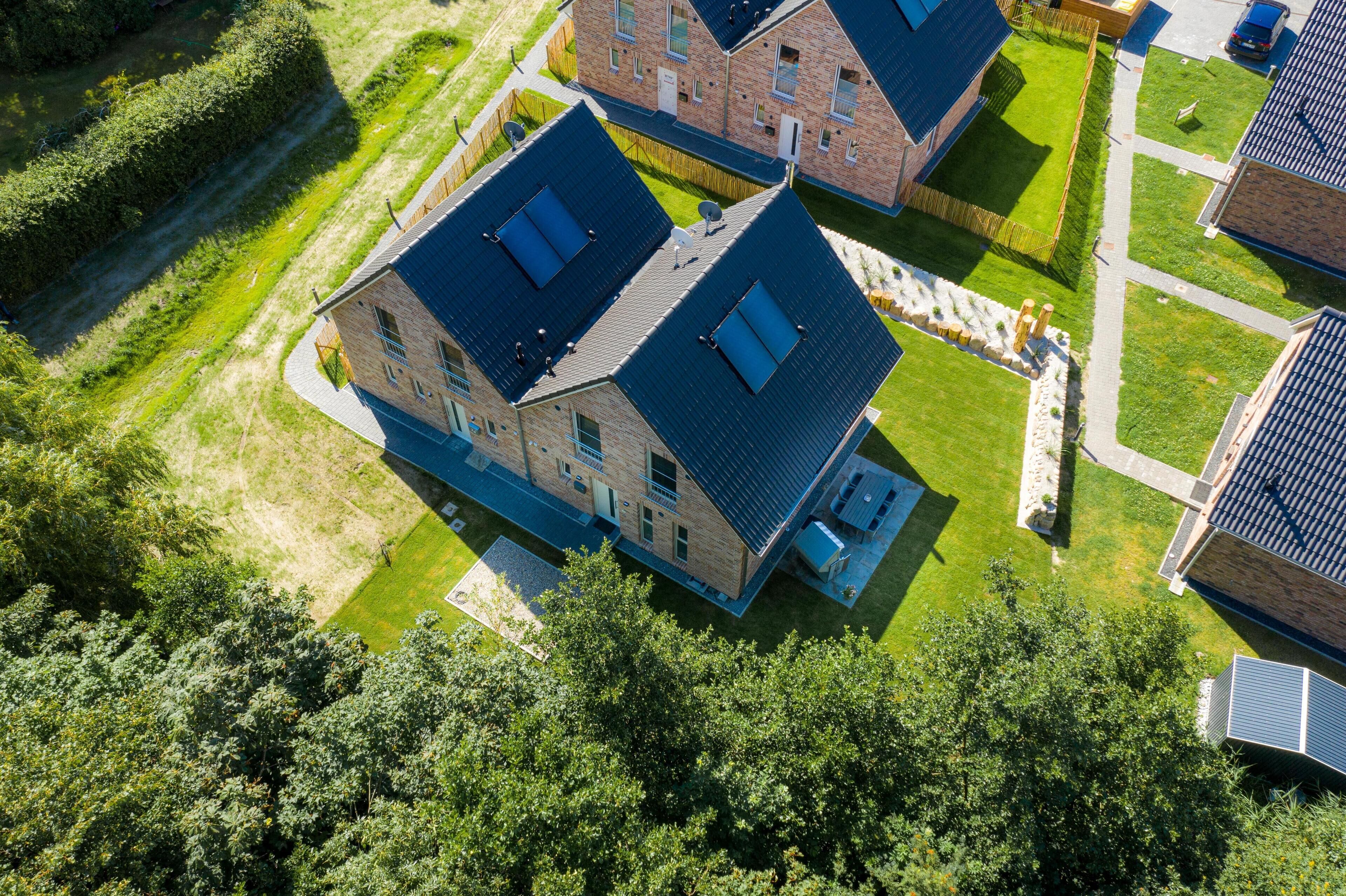 Luchtbeeld van een woongebied met twee bakstenen huizen, elk met een donker dak en zonnepanelen.