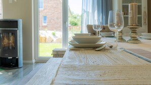 A dining table set with white plates, bowls, and wine glasses, with a candle holder and a fireplace in the background. - Ferienhaushälfte "zweite Heimat" in Tating für 6 Personen (Tating)