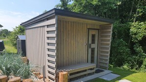 A wooden outdoor structure with a door and a small porch, surrounded by a garden with wooden posts and grass. - Ferienhaushälfte "zweite Heimat" in Tating für 6 Personen (Tating)