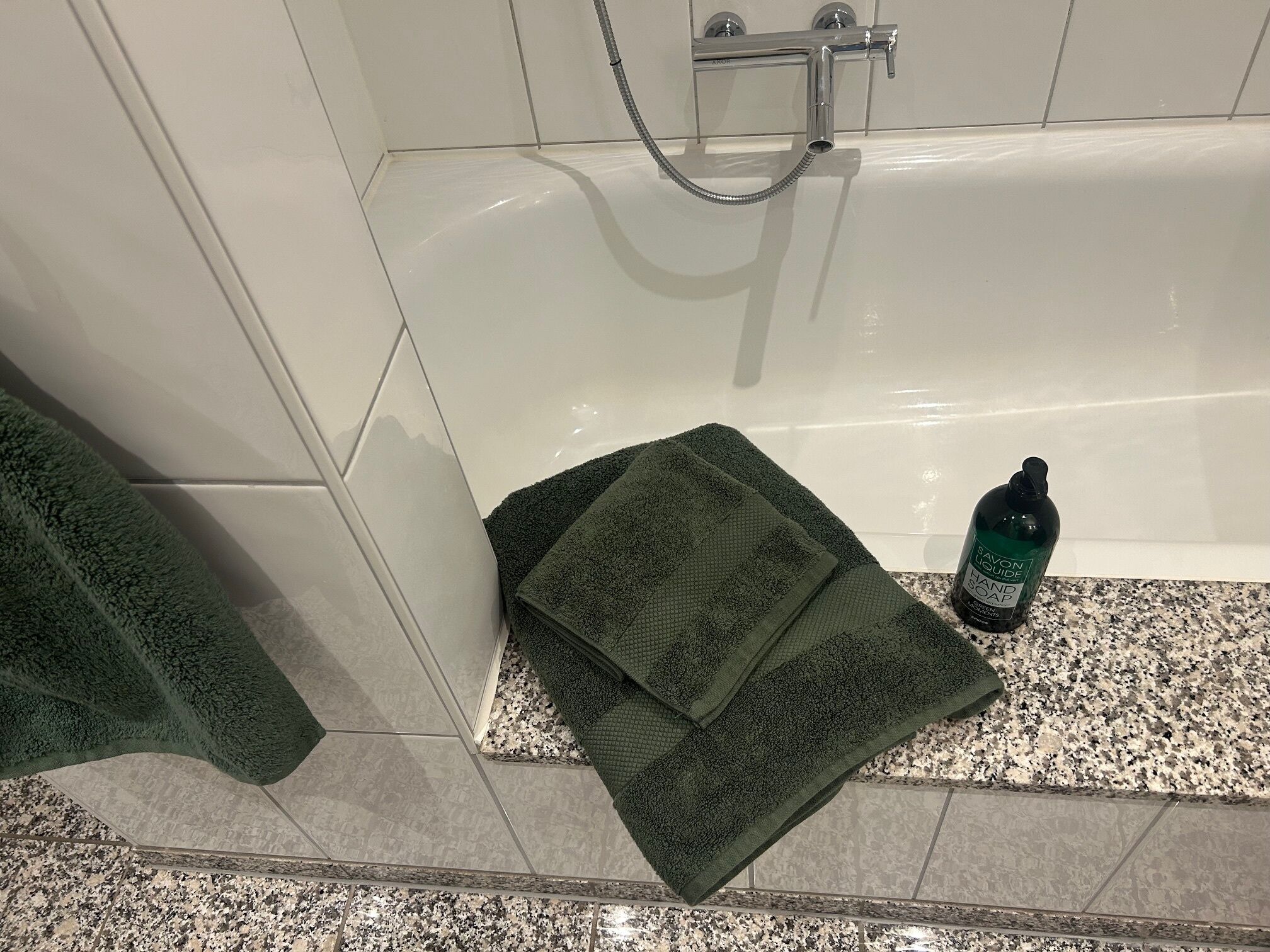 A bathroom with a white bathtub, a green bath mat, and a bottle of hand soap on the floor.
