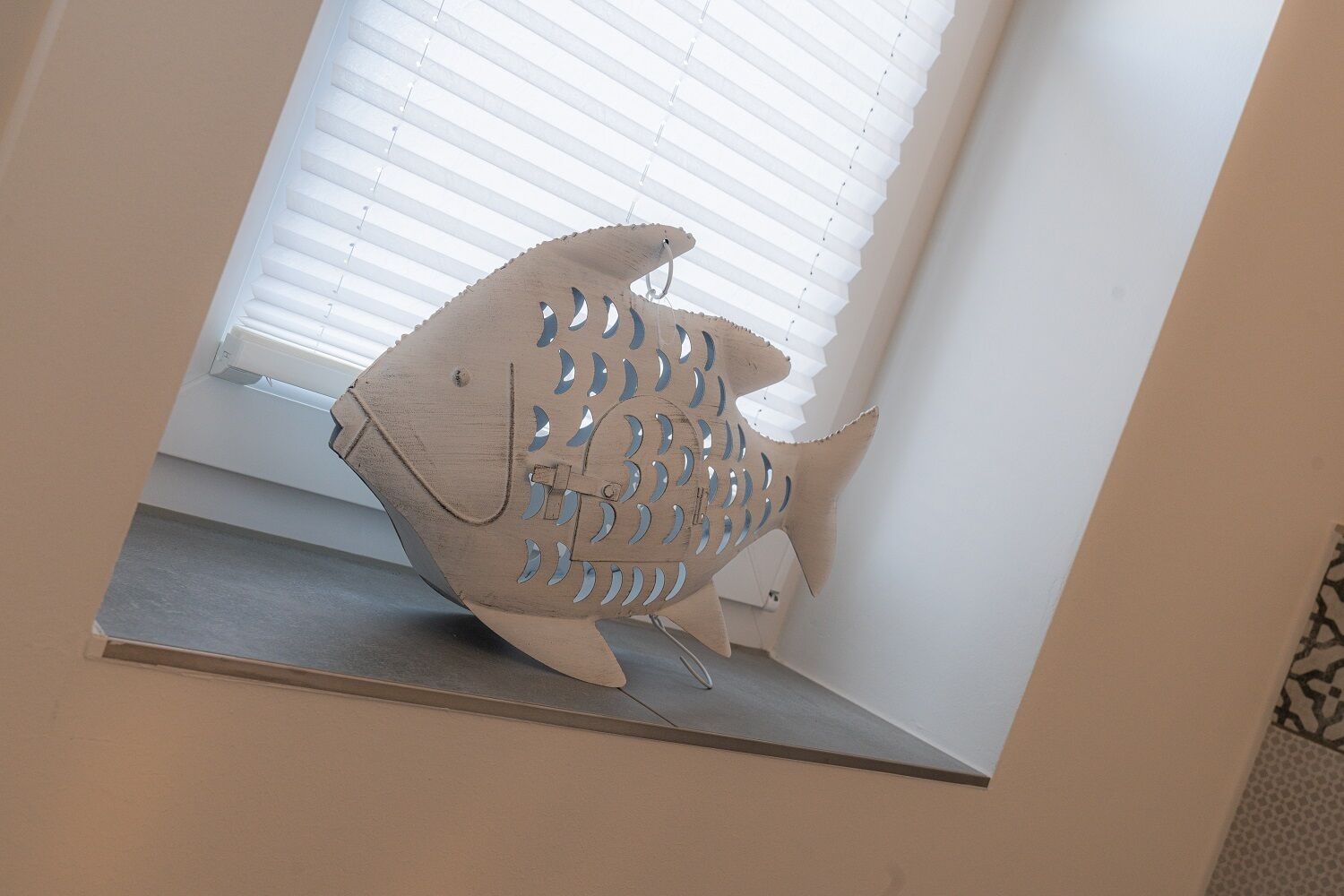 Una escultura con forma de pez sobre una estantería junto a una ventana con persianas.