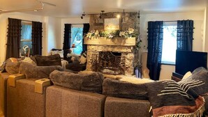 A cozy living room with a stone fireplace, a sectional sofa, and a television. - New! Secluded Cabin w/ Hot Tub, close to Solitude & Brighton Ski Resorts (Brighton)