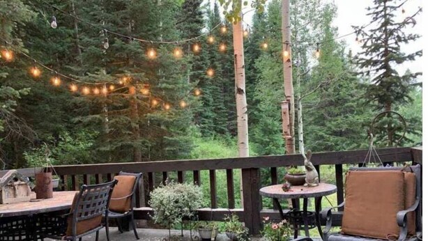 An outdoor deck with wooden flooring, metal chairs, a round table, and string lights. - New! Secluded Cabin w/ Hot Tub, close to Solitude & Brighton Ski Resorts (Brighton)