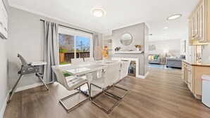 A modern kitchen with white cabinets, a dining area with a white table and chairs, and a view of the outdoors. - South SJ 4BR: Spacious & Comfy (San Jose)