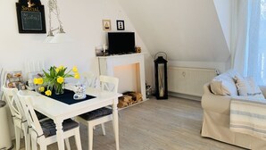Een gezellige woonkamer met een witte eettafel, stoelen, een open haard, een bank en een televisie op een dressoir.