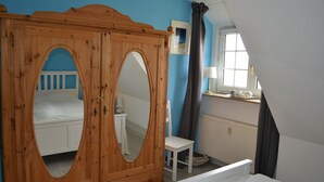 Een slaapkamer met een houten garderobe, een wit bed, een stoel, een raam met gordijnen en een radiator.
