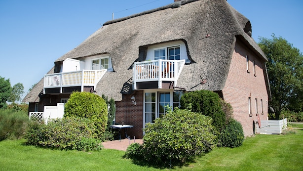 Een rieten huis met een balkon, omgeven door groen.