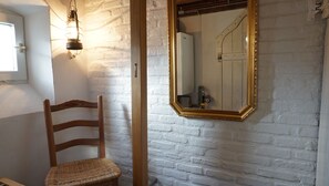 A room with a white brick wall, a wooden chair, a mirror with a gold frame, and a light fixture.