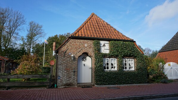A traditional brick building with a tiled roof, ivy-covered walls, and a white door.