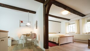 Ein Schlafzimmer mit einem hölzernen Bett, einem Schreibtisch mit Stuhl, einem kleinen Regal und einem Fenster mit Vorhängen.