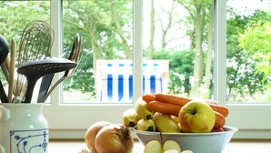 Een keukentafel met een schaal fruit, een hele ui en een witte keramieken kan met keukengerei.