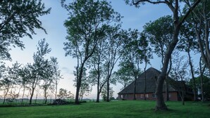 A rural landscape with a thatched-roof house surrounded by trees and a grassy field. - Ferienwohnung "haubarg Windschuur 4" in Welt für 2 Personen (Welt)