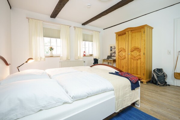 A bedroom with a large bed, wooden wardrobe, and a desk with a chair.
