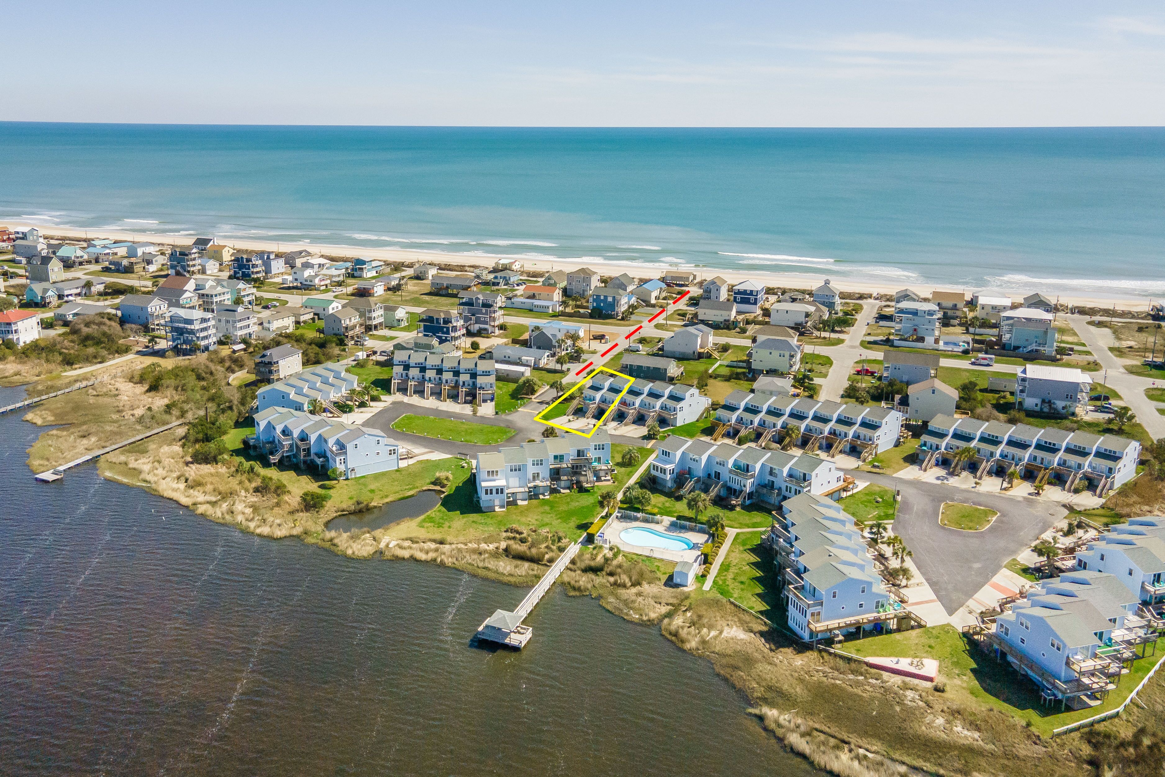 An aerial view of a coastal residential area with houses, a dock, and a beach.