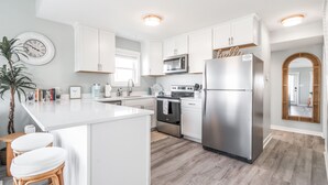 Una cocina moderna con armarios blancos, electrodomésticos de acero inoxidable y una isla central con taburetes.