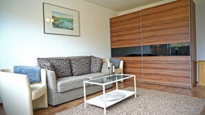 A modern living room with a sofa, a glass coffee table, and a wooden wardrobe. - Appartement "rochelsand EG" in Tating für 1-3 Personen (Tating)