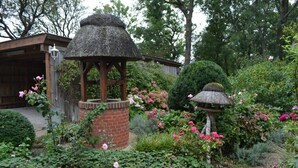 A garden with a gazebo, a brick structure, and various flowering plants. - Rosenkate in Garding: 130 m² space for 5 people (Garding)