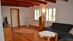 A living room with a wooden floor, a grey sofa, a small wooden table, and a TV on a stand. - Rosenkate in Garding: 130 m² space for 5 people (Garding)
