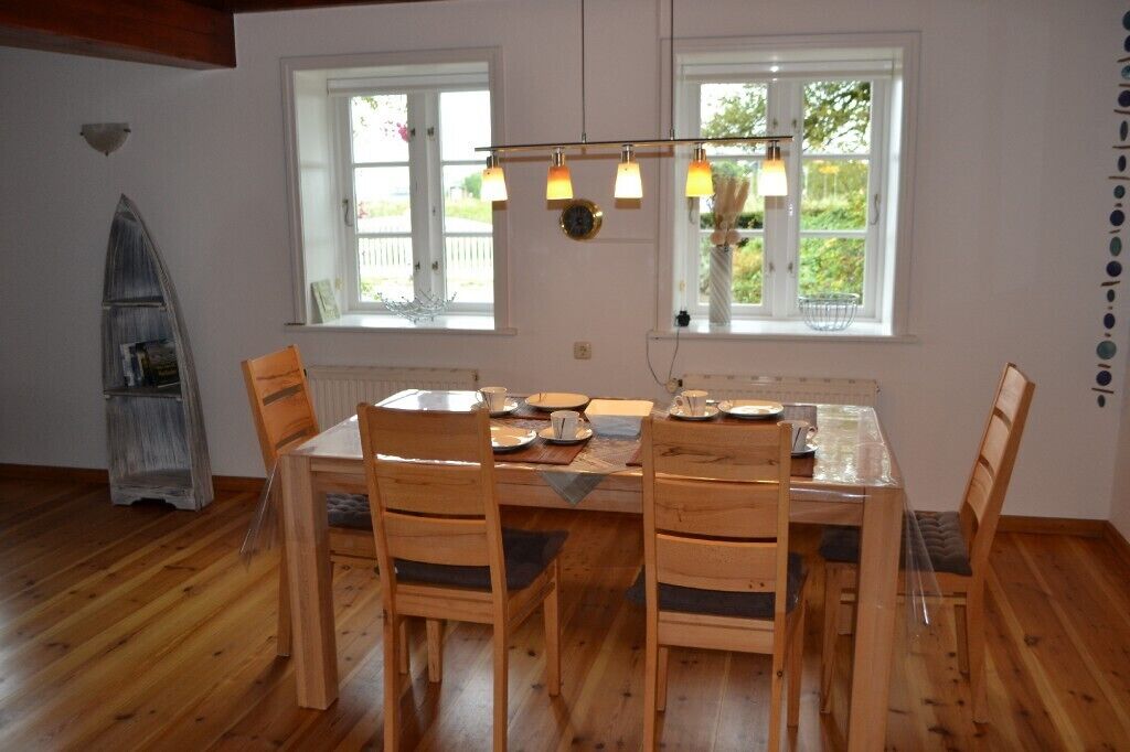 A dining area with a wooden table and chairs, a chandelier, and windows with views of greenery.
