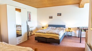 A bedroom with a bed, bedside tables, a mirror, a wardrobe, and a small table with a foosball table. - Ferienwohnung auf dem Ferienhof Nickelswarft 2 in Poppenbüll für 2-6 Personen (Poppenbüll)