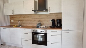 A modern kitchen with white cabinets, a stainless steel oven, a coffee maker, and a kettle. - Ferienwohnung auf dem Ferienhof Nickelswarft 2 in Poppenbüll für 2-6 Personen (Poppenbüll)