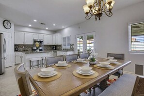 A modern kitchen with white cabinets, granite countertops, and a dining area with a wooden table set for six. - Dulce Vida: Pool, Spa, Table Games, Fire Pit, BBQ! (Indio)