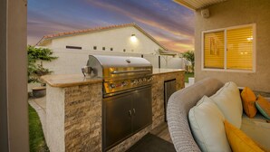 Une cuisine extérieure équipée d’un barbecue, d’un four encastré et d’un plan de travail en pierre.