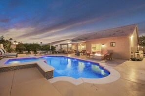 Una piscina con una zona de estar hundida, rodeada de sillones de descanso y un patio con mobiliario exterior.