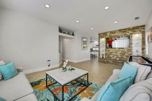 A spacious living area with a sofa, coffee table, and a kitchen in the background. - Dulce Vida: Pool, Spa, Table Games, Fire Pit, BBQ! (Indio)