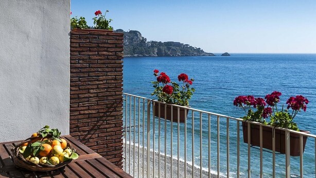 A balcony with a view of the sea, a brick wall, and potted red flowers. - Casa Annabella Bilo - Waterfront apartment (Giardini Naxos)