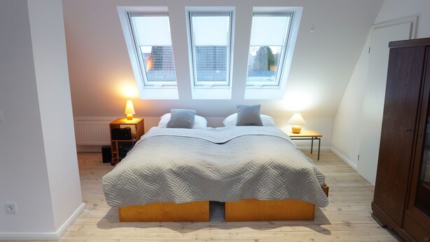 A bedroom with a large bed, two bedside lamps, a wooden wardrobe, and a skylight.