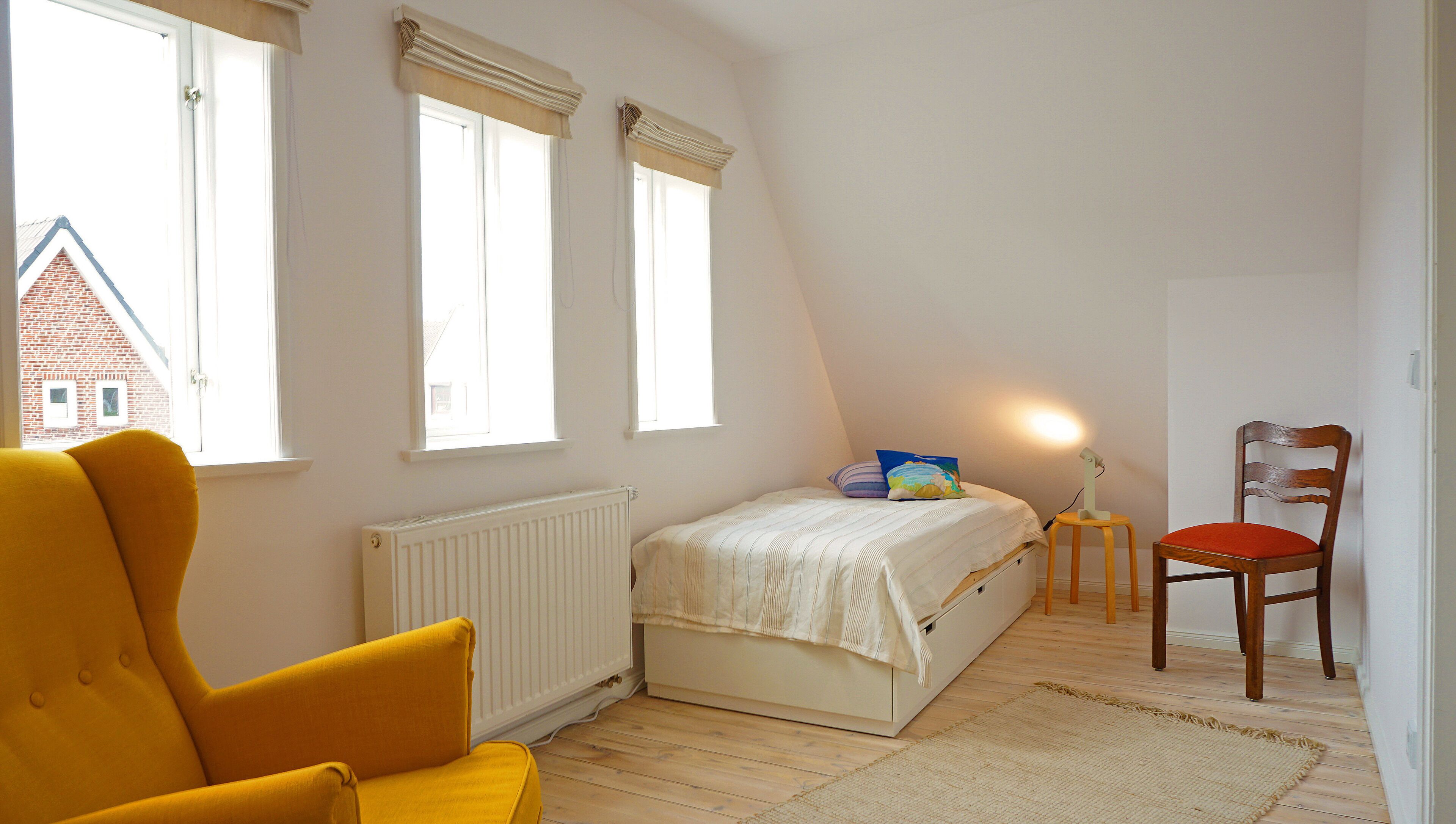 Een slaapkamer met een bed, een stoel, een radiator en twee ramen.