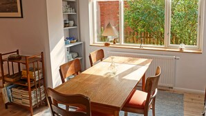 A dining area with a wooden table and chairs, a bookshelf, and a window with a view of greenery.